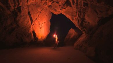A lone adventurer illuminates a vast Californian cave with a torch at night.