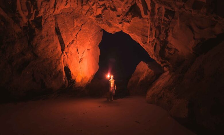 A lone adventurer illuminates a vast Californian cave with a torch at night.
